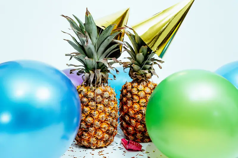 two pineapples wearing party hats and surrounded by balloons