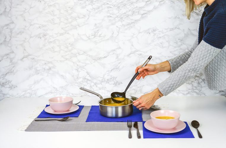 a woman pouring the pumpkin soup from the pot into a bowl