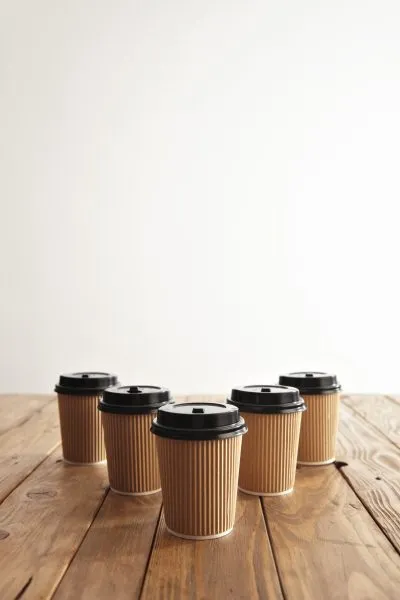 Five carton paper cups with black caps in row isolated on center of rustic wooden table, top view